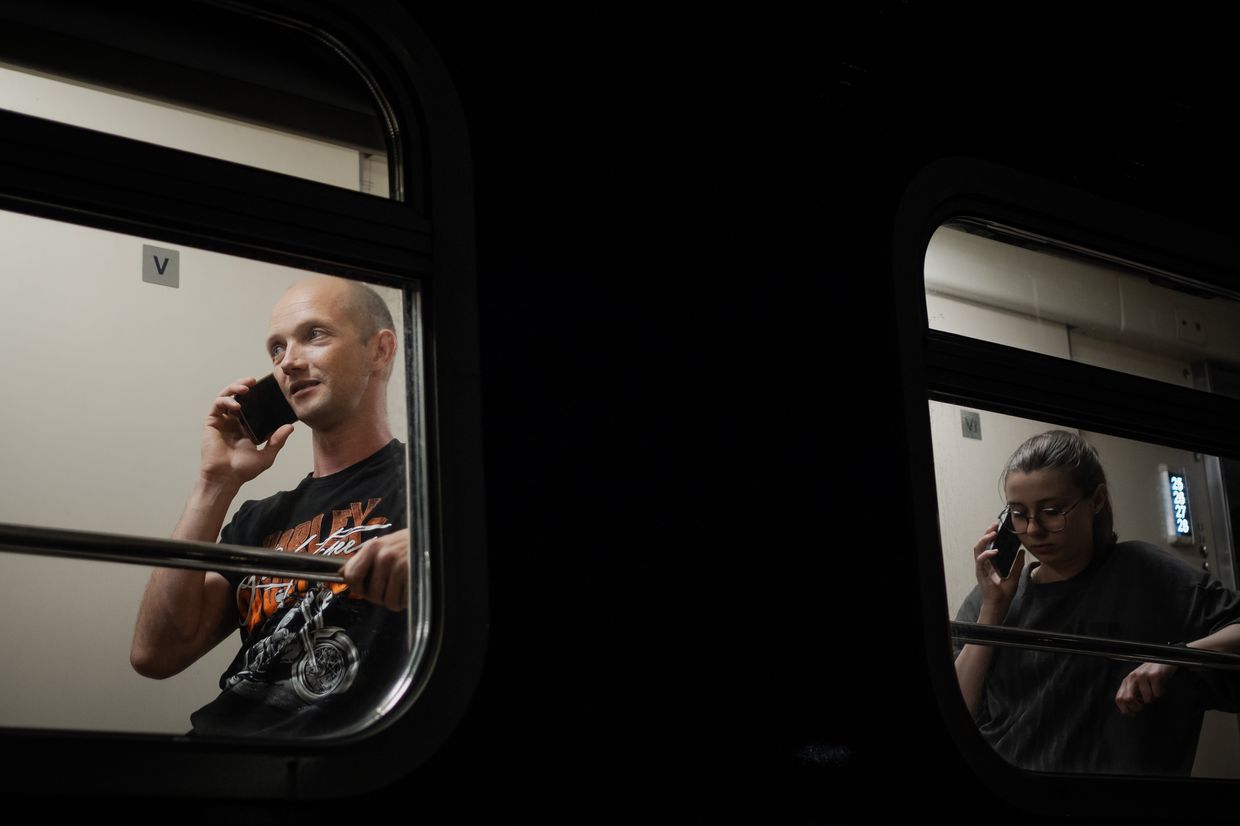 People talk on the phones inside the train on the railway station in Kyiv