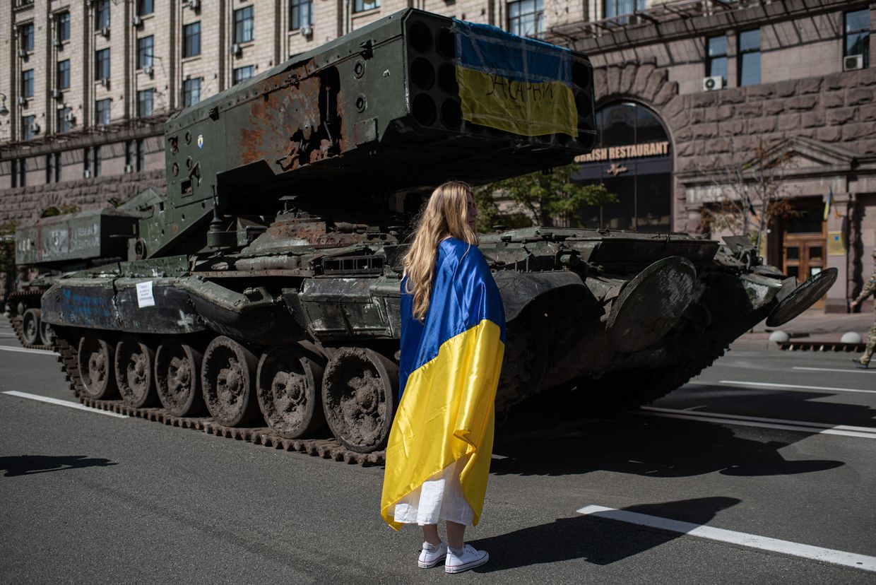 A young woman wrapped in the Ukrainian national flag walks next to the burnt Russian military vehicles in Kyiv