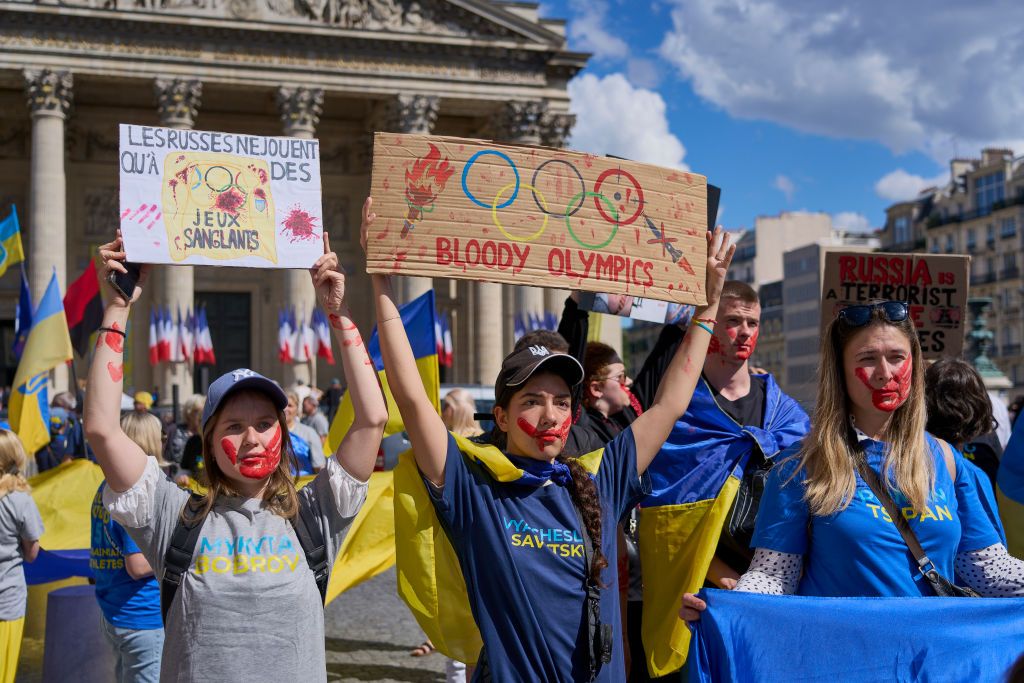 A woman holds a sign with the text "Bloody Olympics" during a march in memory of the hundreds of Ukrainian athletes 