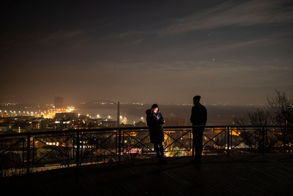 A man looks over Kyiv as a woman looks at her phone