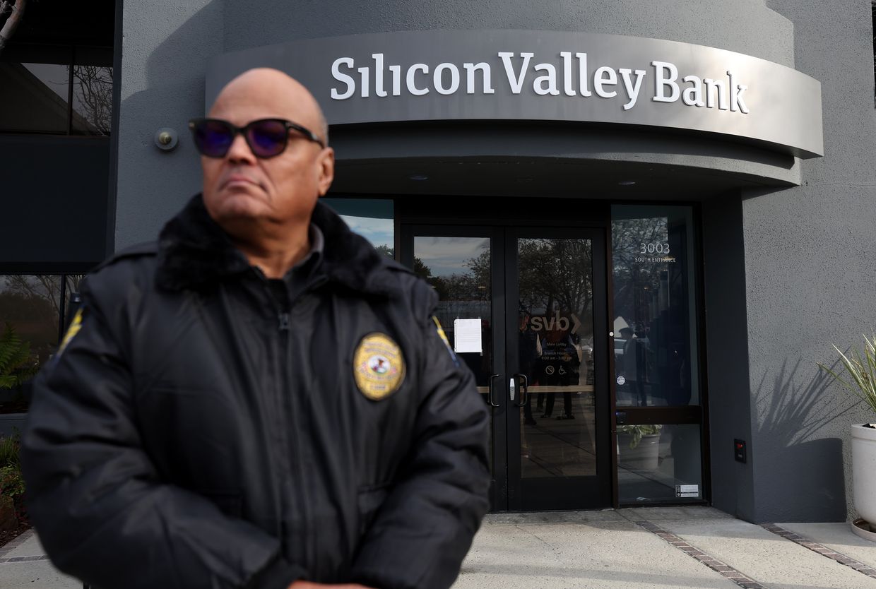 A security guard at Silicon Valley Bank monitors a line of people outside the office in Santa Clara