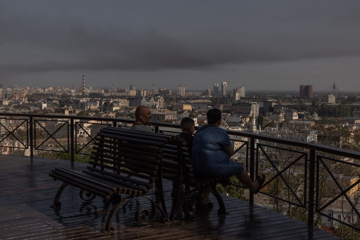A man, a woman and a child look on as smoke rises over buildings in Kyiv, Ukraine, on Aug. 26, 2024. 