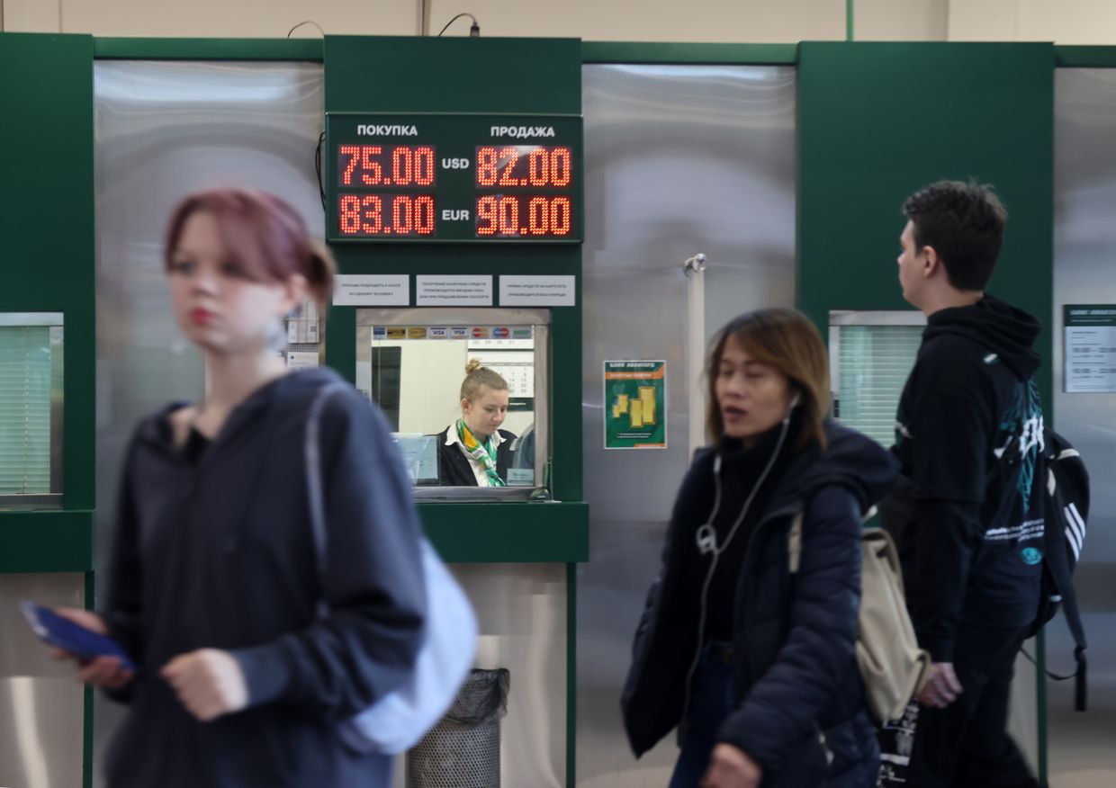 A cashier was seen in the exchange banking office with a panel of rates of the US dollar and other currencies to the ruble