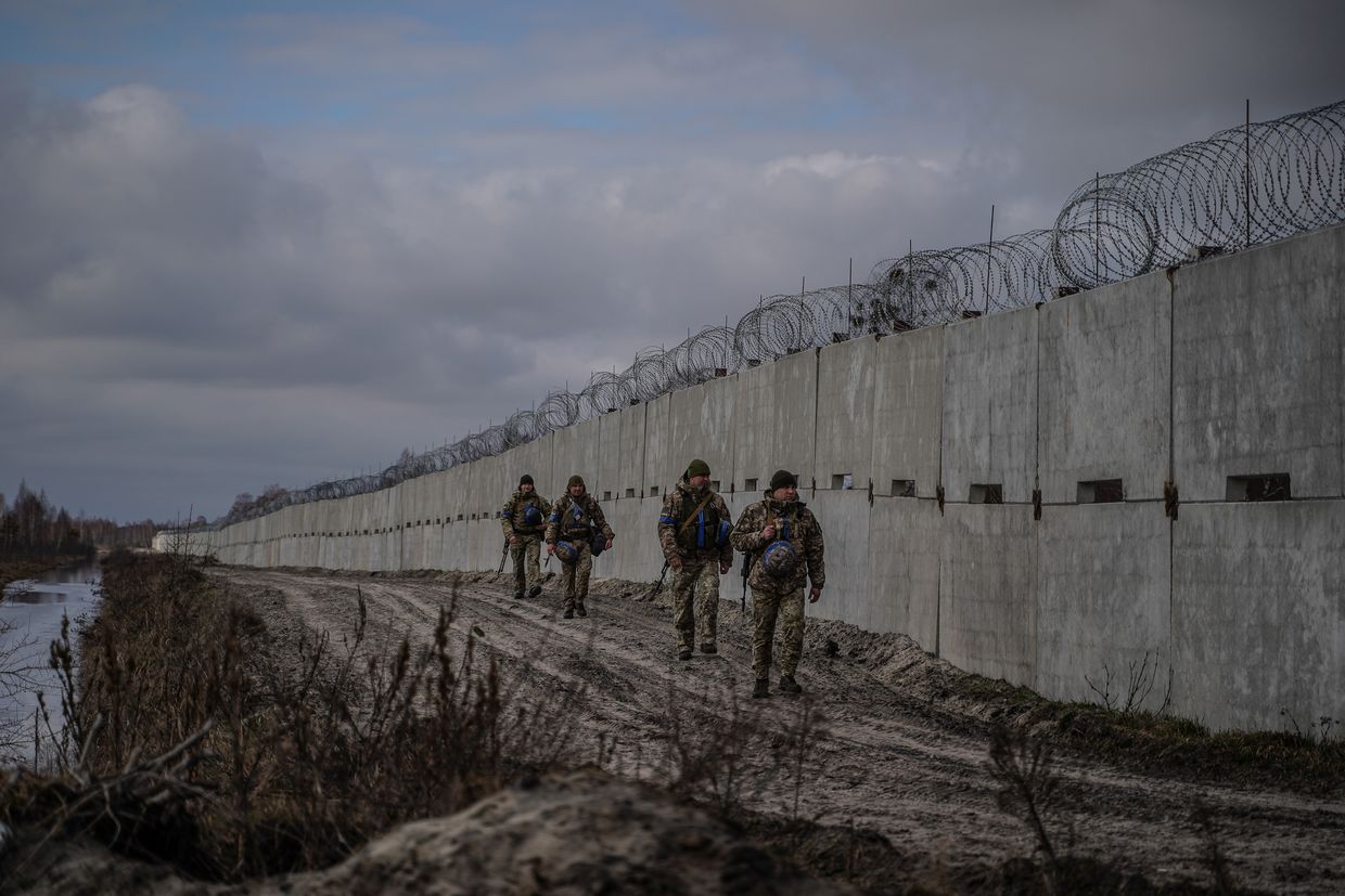 Ukrainian border guards walk past concrete barrier during patrolling of the border with Belarus in Volyn Oblast