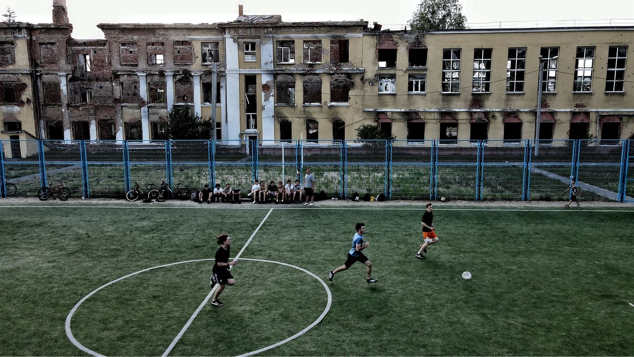 teenagers play football on a pitch in front of a school building destroyed due to hostilities in Kharkiv, Ukraine on June 23, 2024