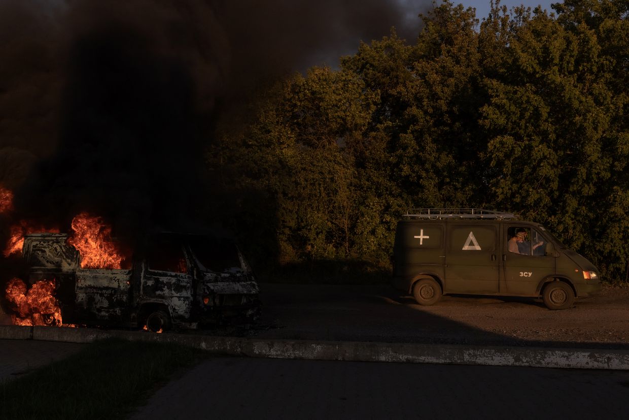 A Ukrainian military vehicle drives past a burning car on a road near the border with Russia in the Sumy region of Ukraine