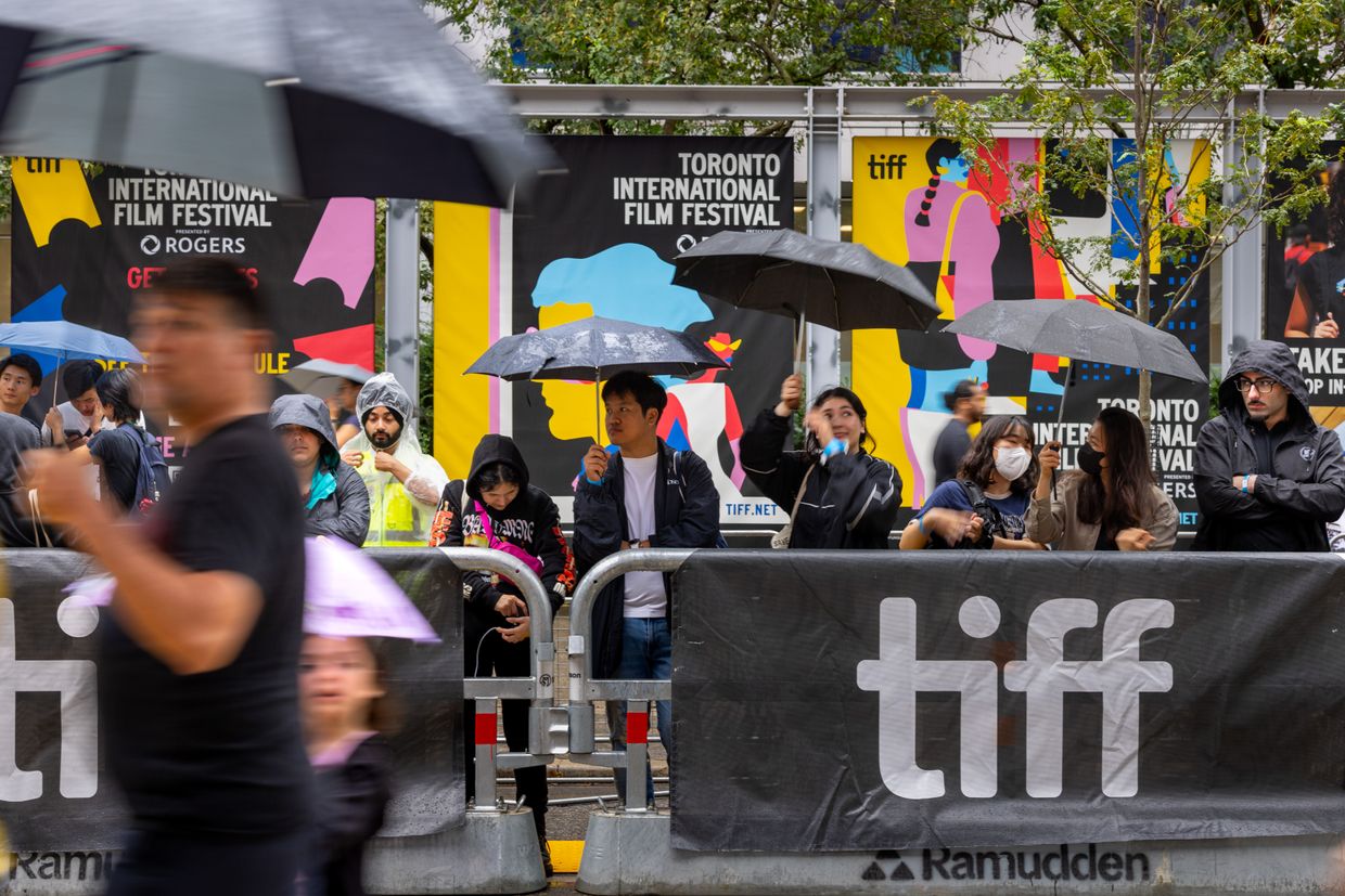 People stand in the rain, waiting for an evening movie premier along King Street W, during the 2024 Toronto International Film Festival in Toronto