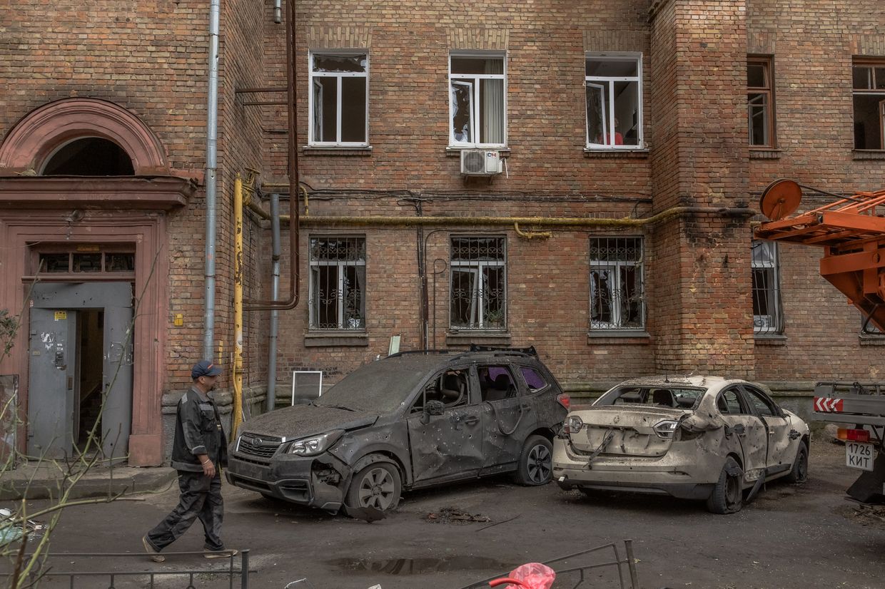 A man walks past cars and a residential building damaged following a Russian drone attack in Kyiv