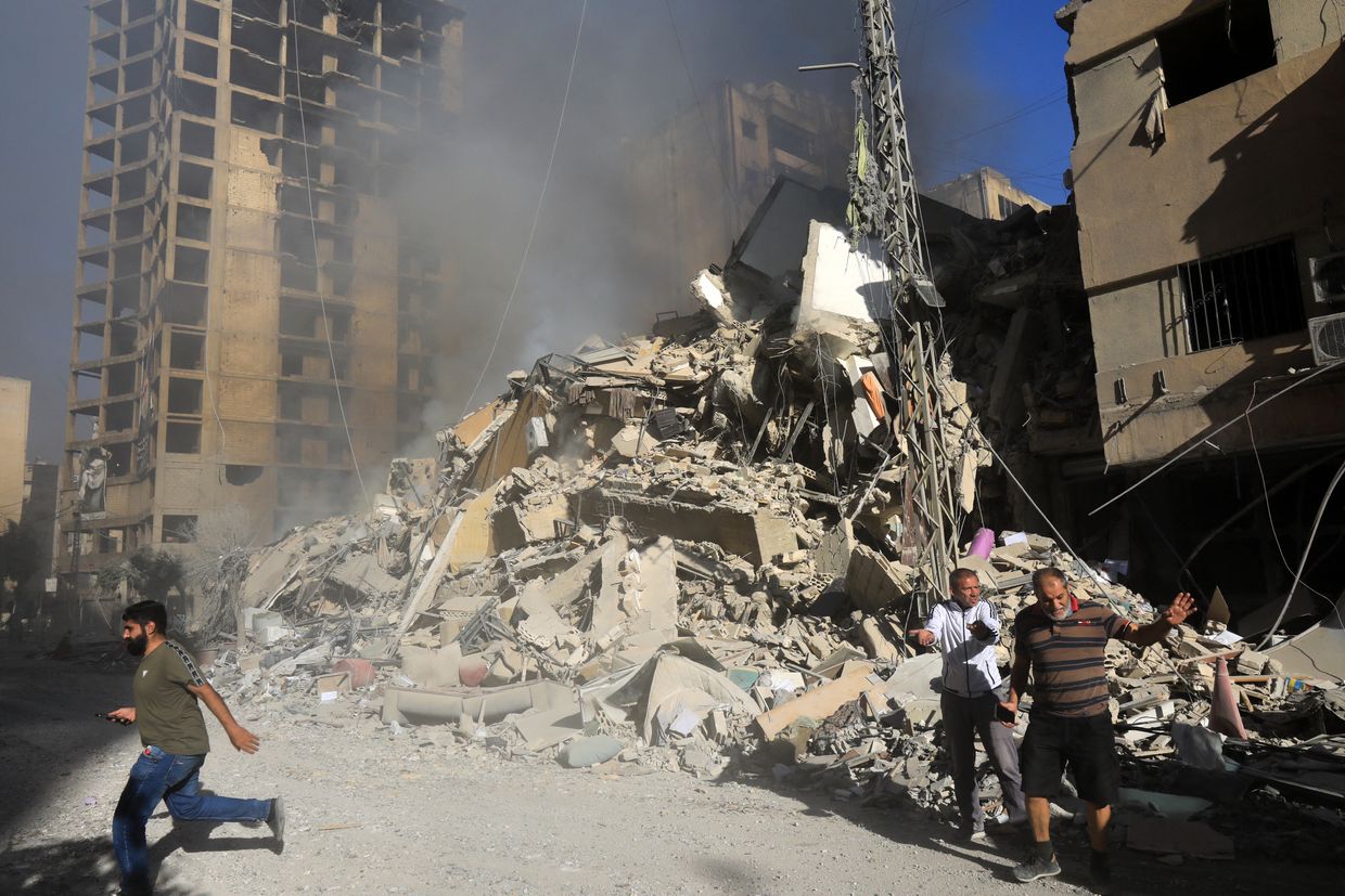 Residents walk in front of a building still smoldering after it was leveled in an overnight Israeli airstrike