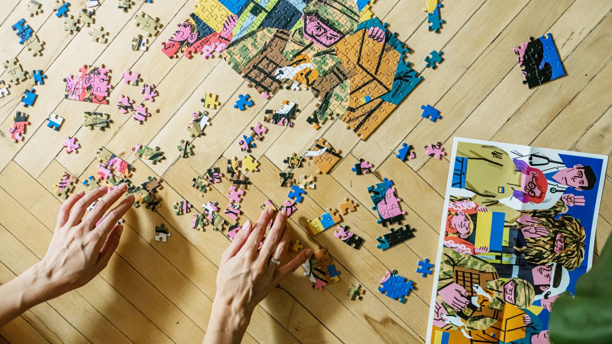 Two hands piece together a puzzle on a wooden floor. 