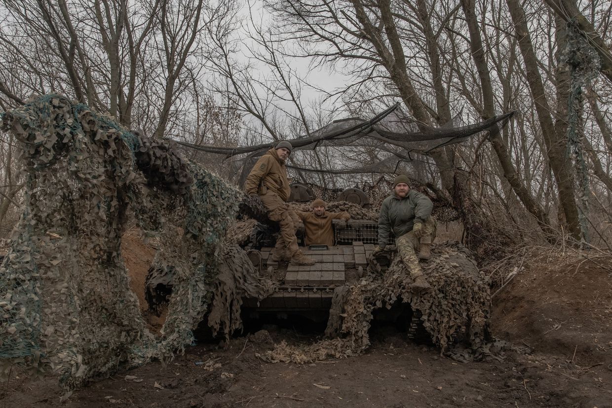 Oleksandr - callsign Statut -(L), 27, Sergiy - call sign Lyozya - (C), 47, and callsign Vardi (R), 27, pose on their tank under a camouflage net near Toretsk, Donetsk Oblast