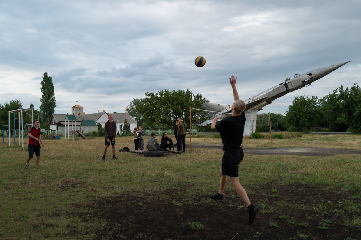 Teenagers play volleyball next to a war memorial in Shostakivka, Donetsk Oblast, Ukraine, on June 16, 2025.
