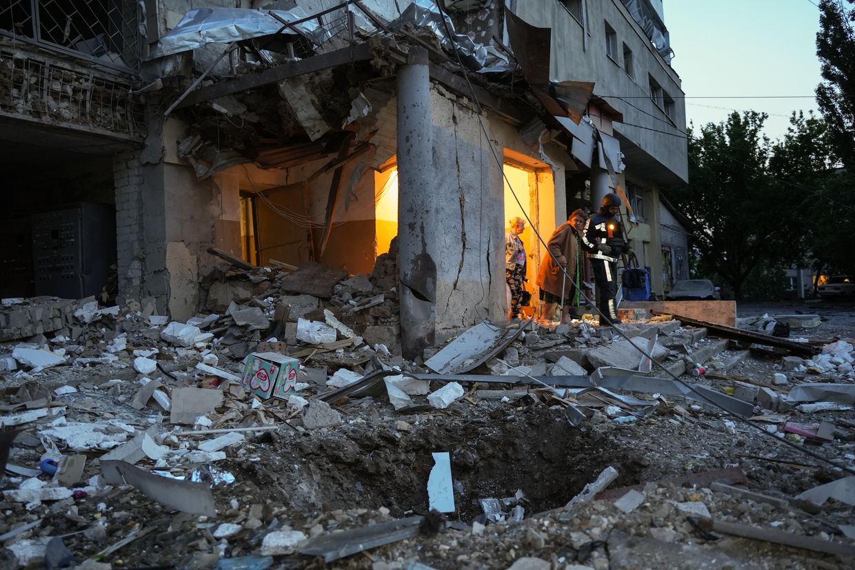 An elderly woman walks with the help of a rescuer amid rubble from a damaged residential building after a Russian drone attack in Kharkiv, Ukraine, on June 12, 2025. 