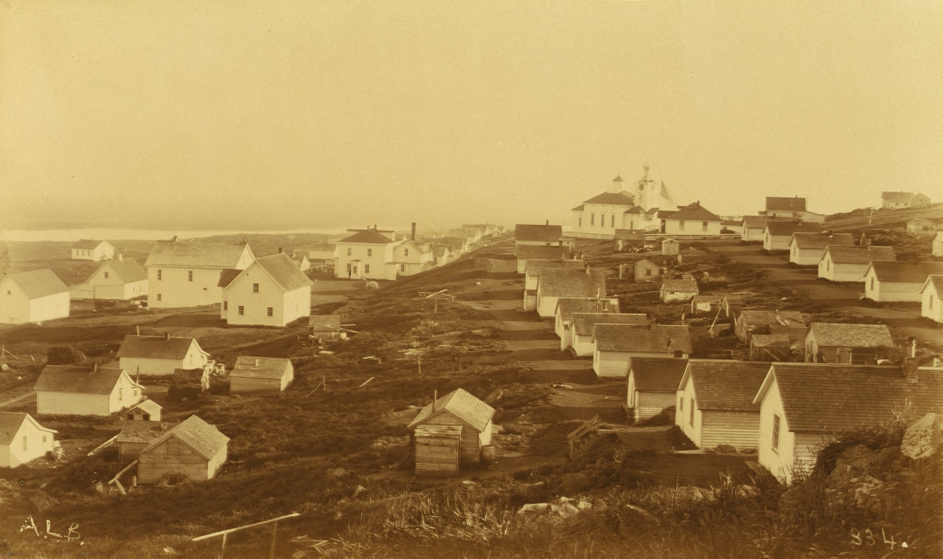 An unidentified village, possibly on Unalaska Island, U.S., with a Russian church featuring a clock in the bell tower in the background, in 1894 or 1895.
