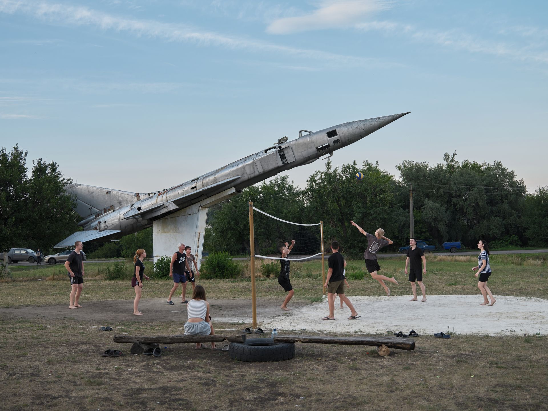 Children play volleyball near the frontline beside a Soviet-era fighter jet monument in eastern Ukraine.